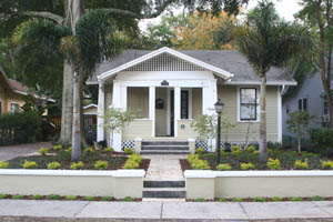 Photo of a bungelow house in the Craftsman style with a wall, patio pavers and landscaping with two palm trees